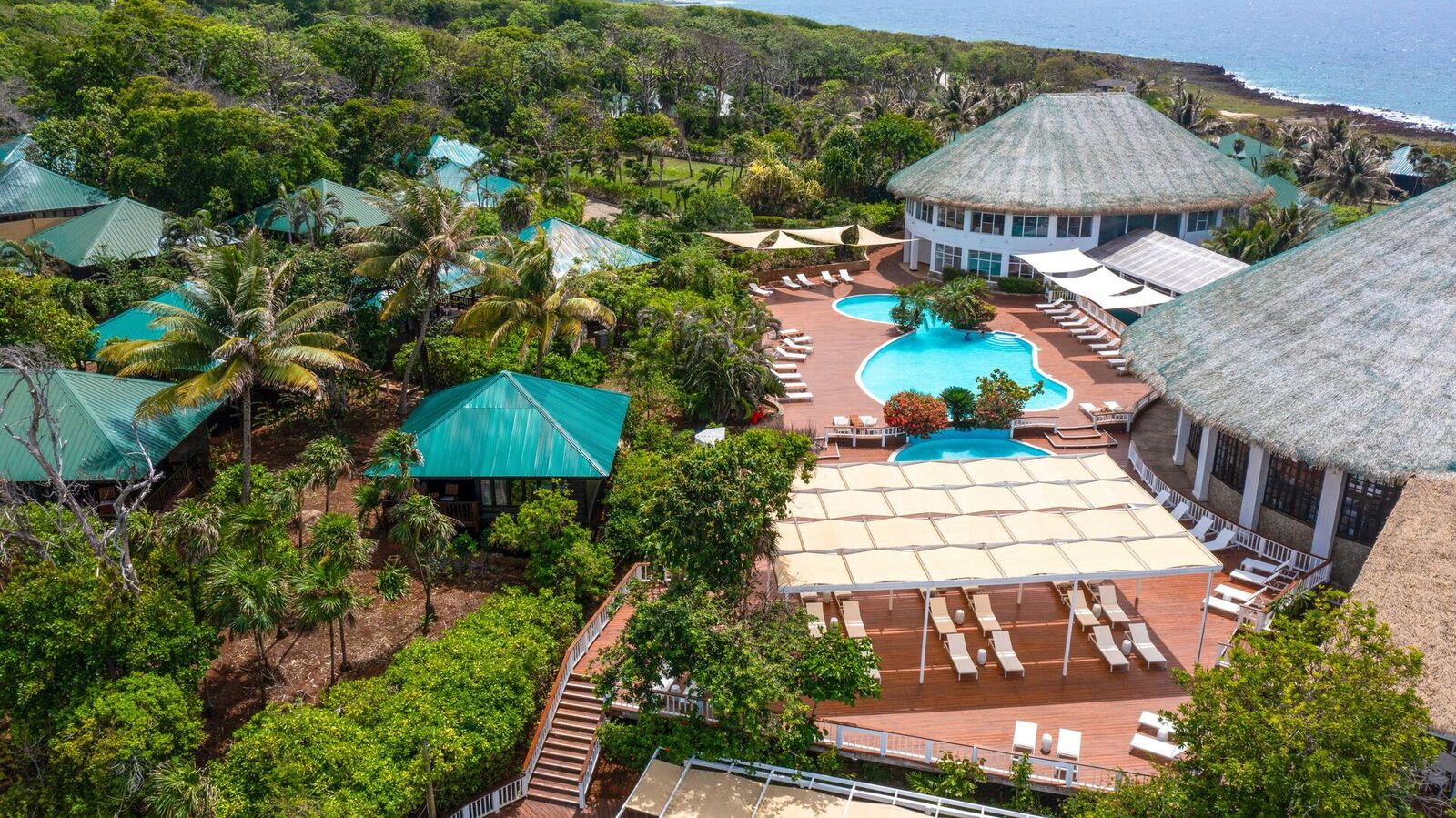 Aerial view of the resort's tropical grounds, pool, and bungalows meeting the ocean