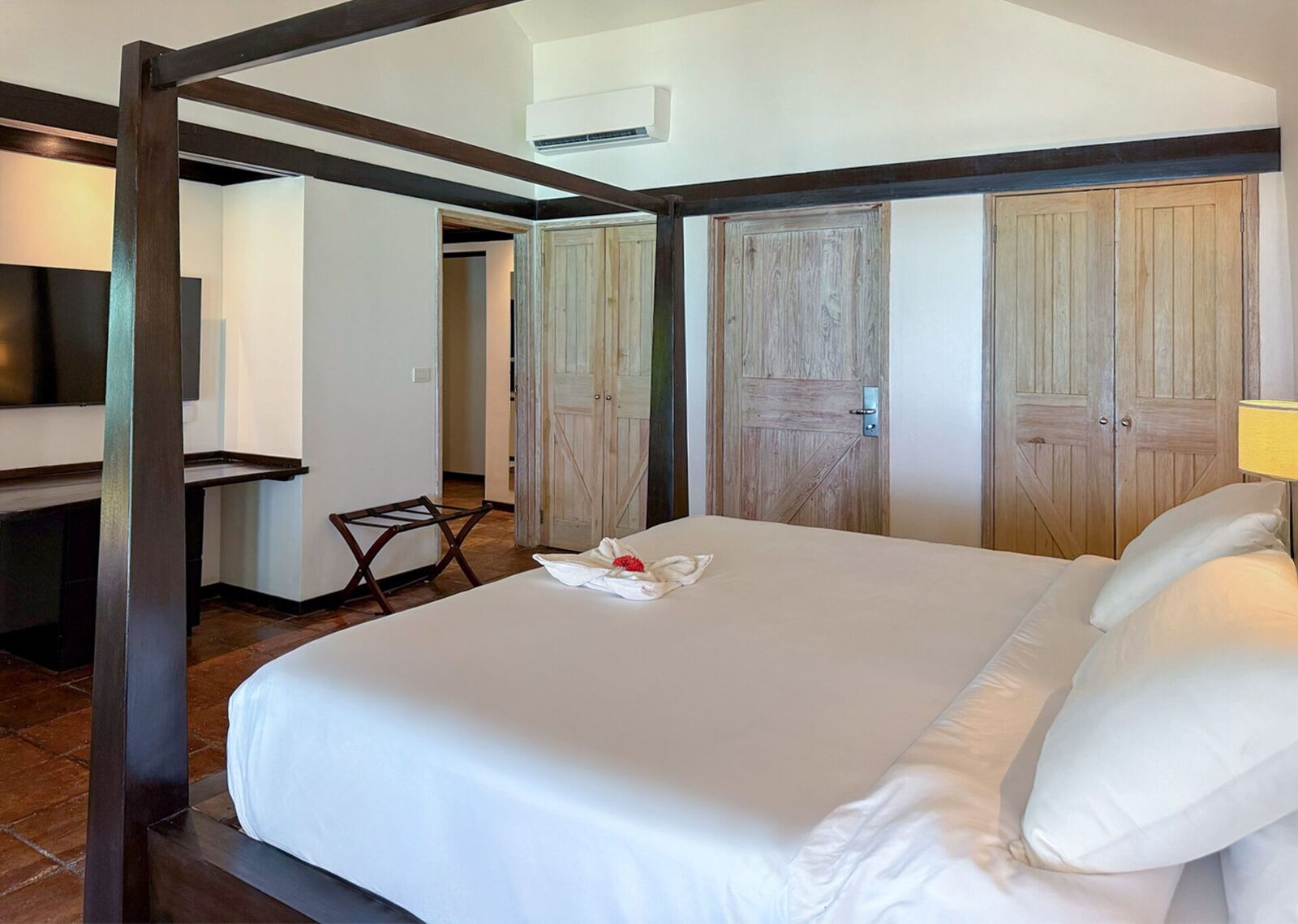 Tropical hotel cabana with a dark wood four-poster bed and white linens