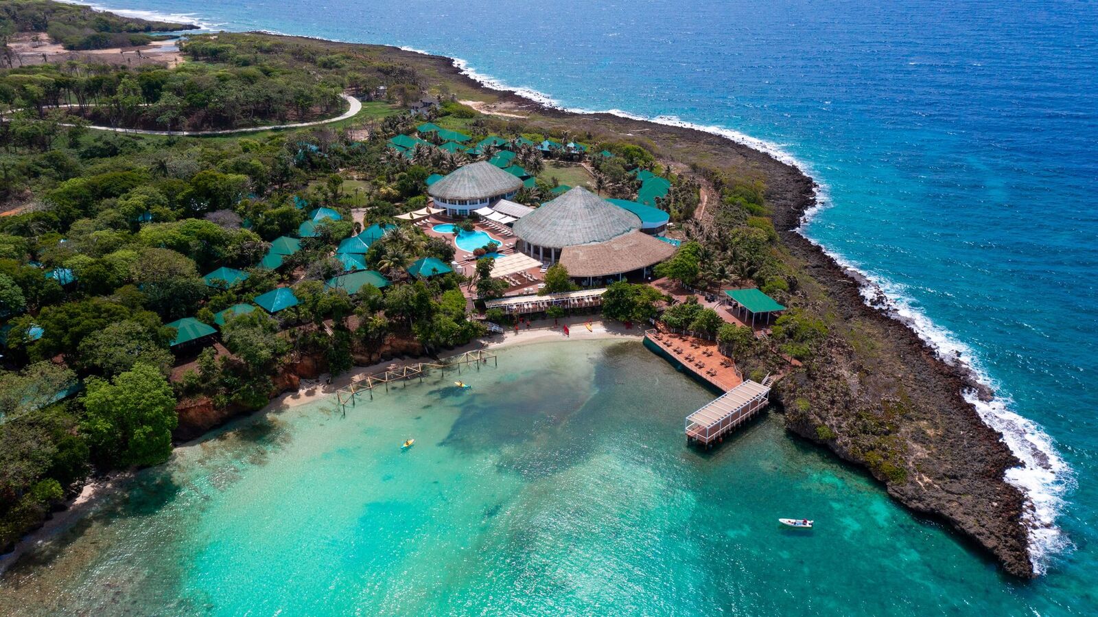 Aerial view of Hotel Roatán Media Luna Resort's thatched-roof cabanas along a turquoise private bay