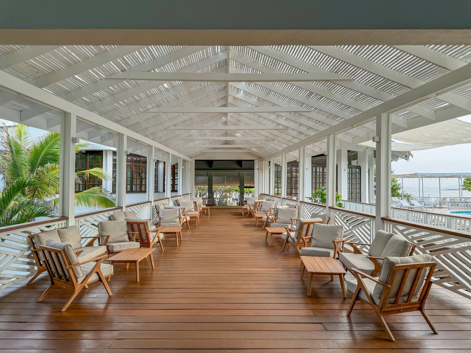 Open-air resort lounge with wooden seating, a white slatted roof, and an ocean view
